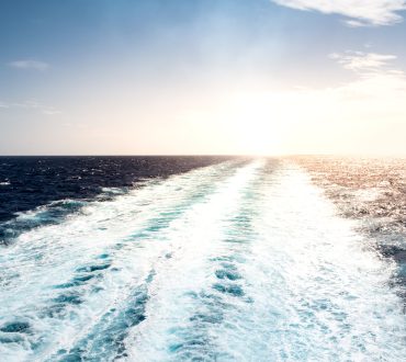 Foamy trail of sailing cruise ship on the Mediterranean Sea on a summer vacation day. No people. Peaceful seascape with small waves, calm sea and sun.
